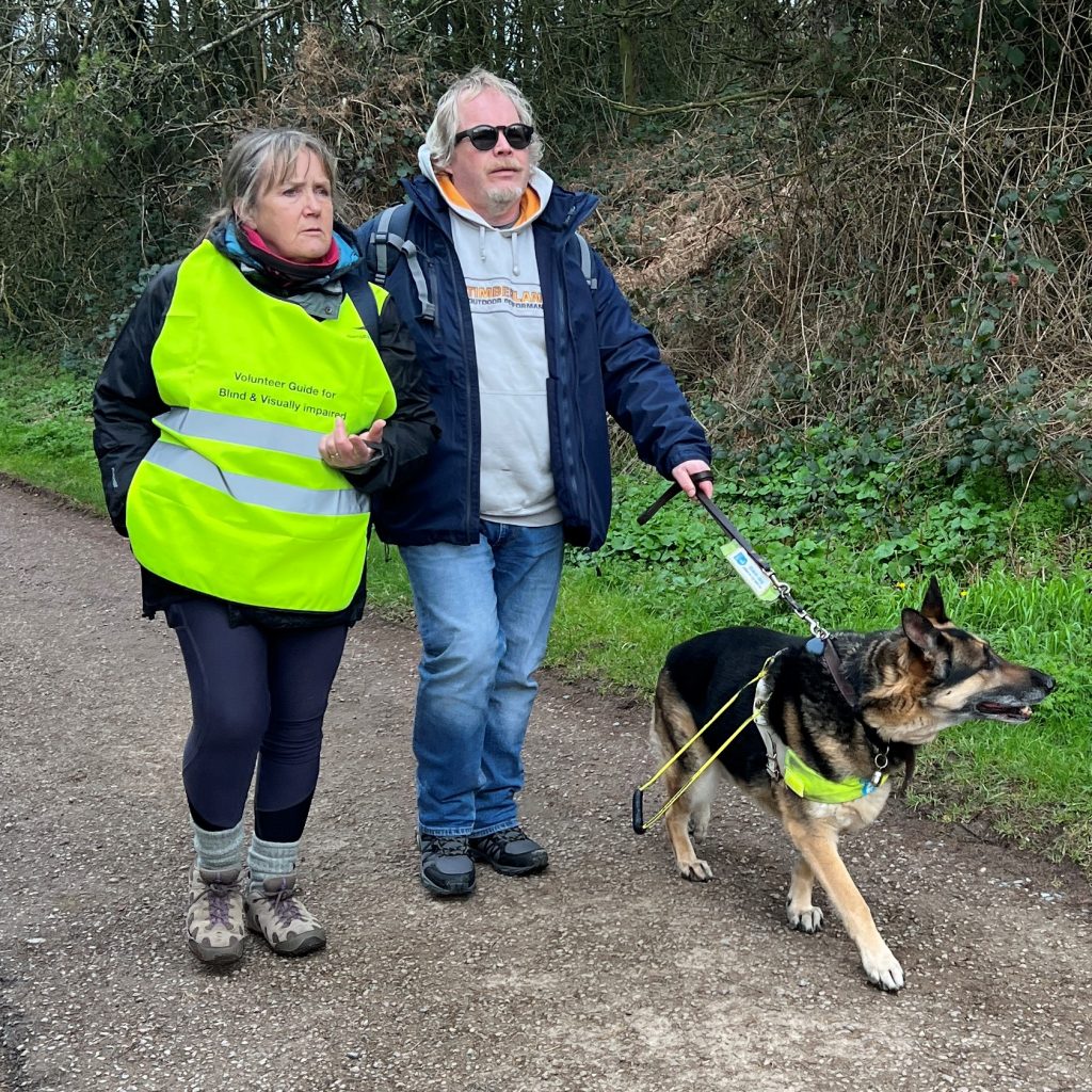 Visually impaired walker being guided by guide-person and guide-dog